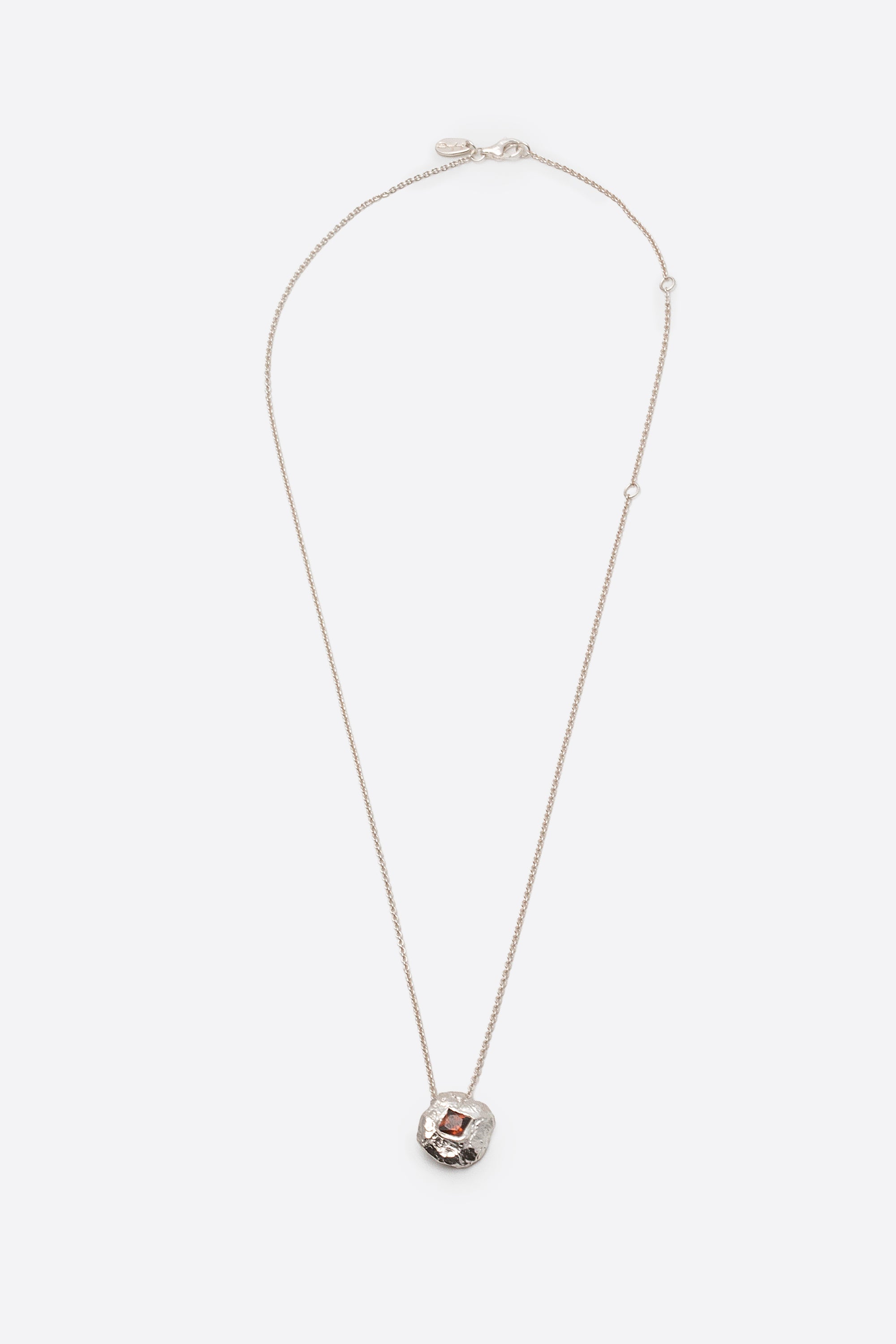 Silver textured round pendant necklace with square red gemstone flat lay
