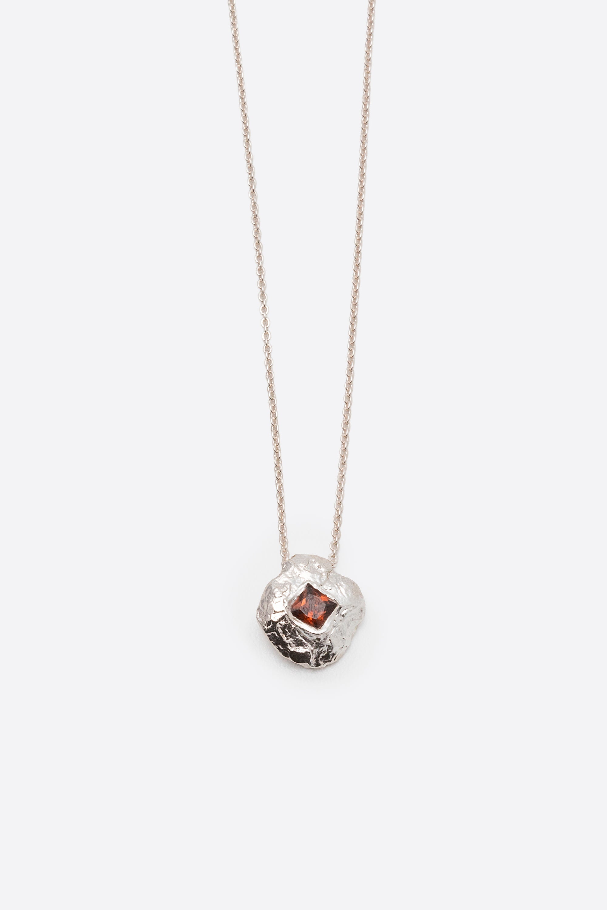 Close-up of silver textured round pendant necklace with square red gemstone