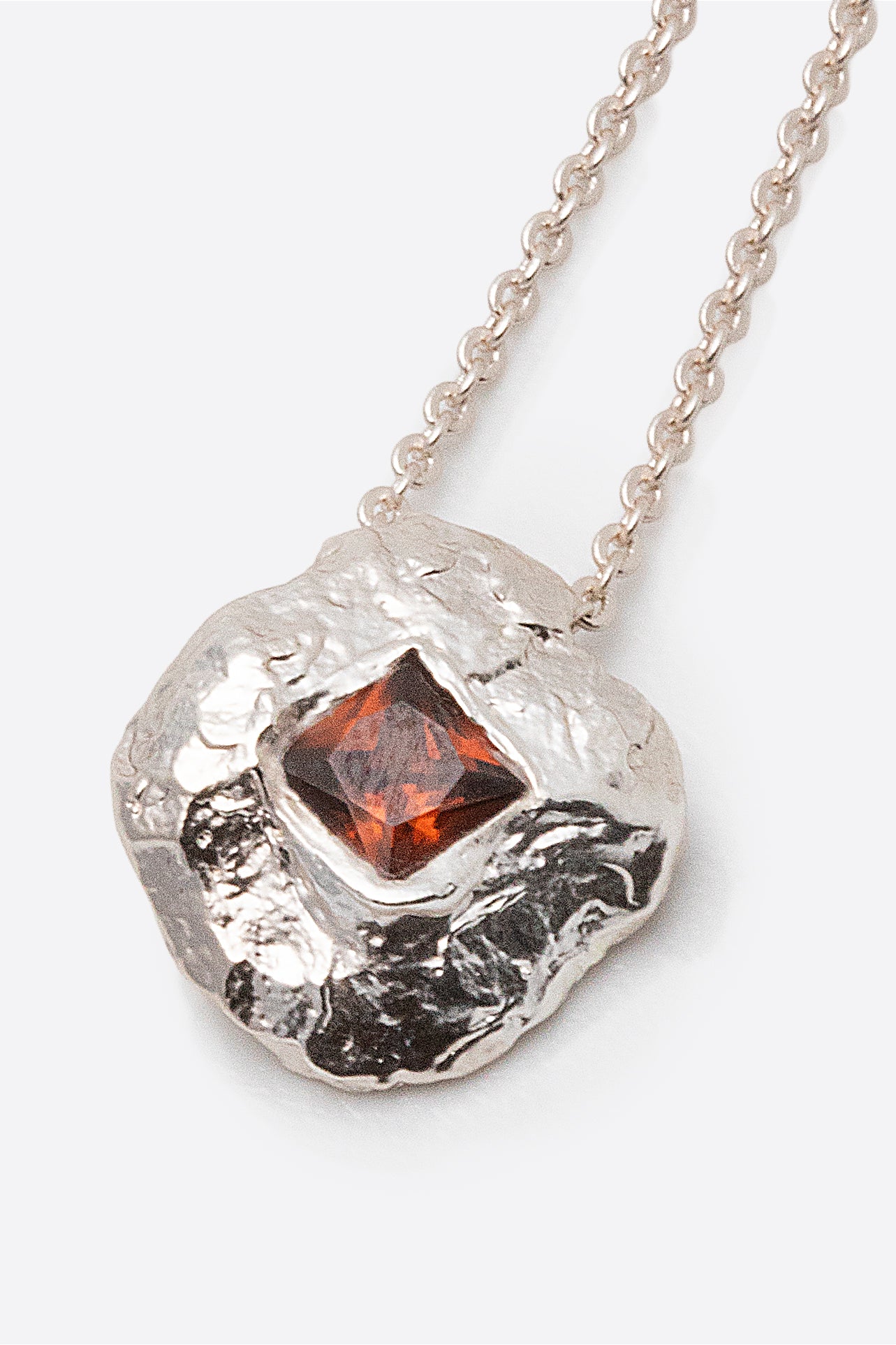 Detail of silver textured round pendant with square red gemstone