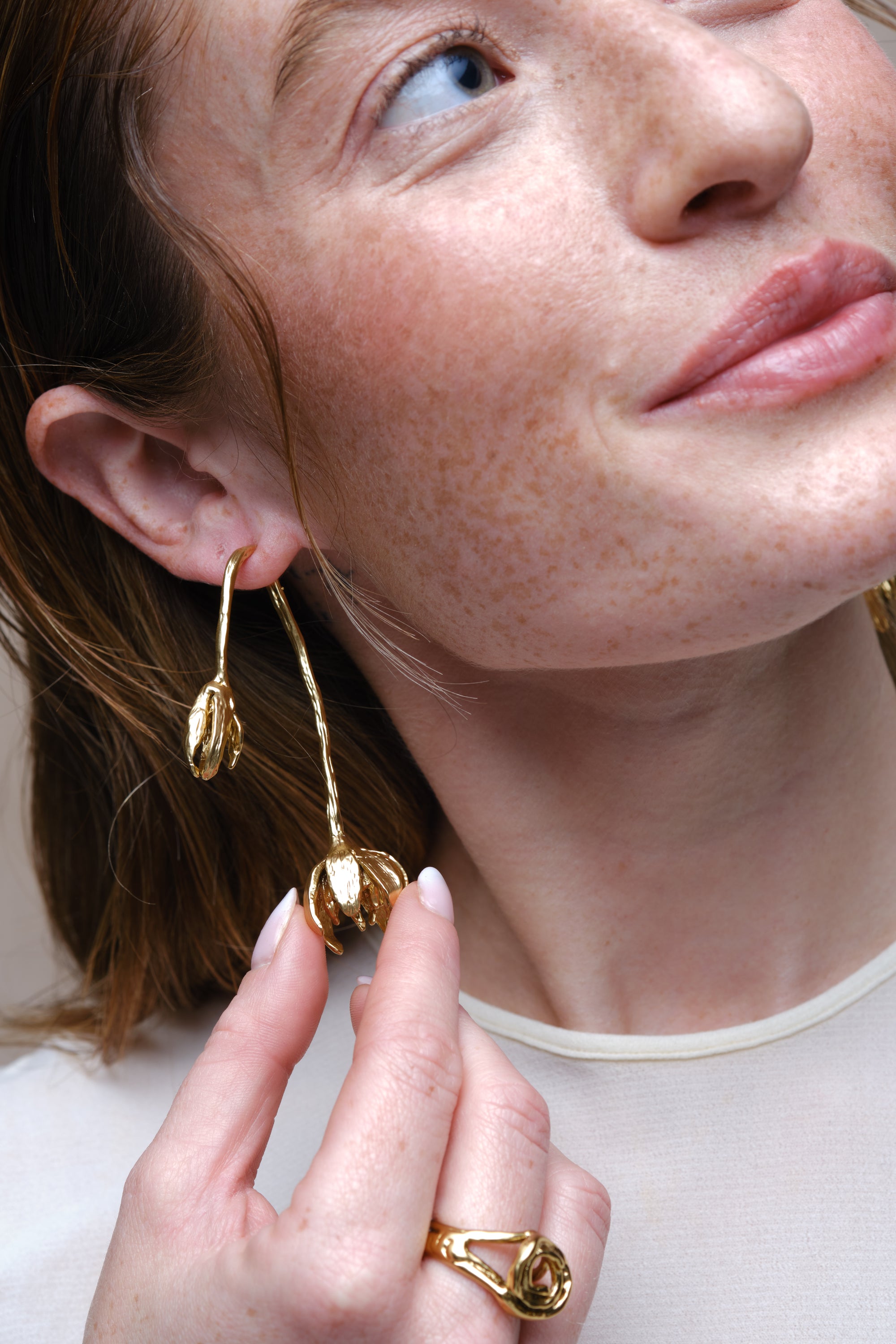 Gold sculptural flower drop earrings worn on model close-up