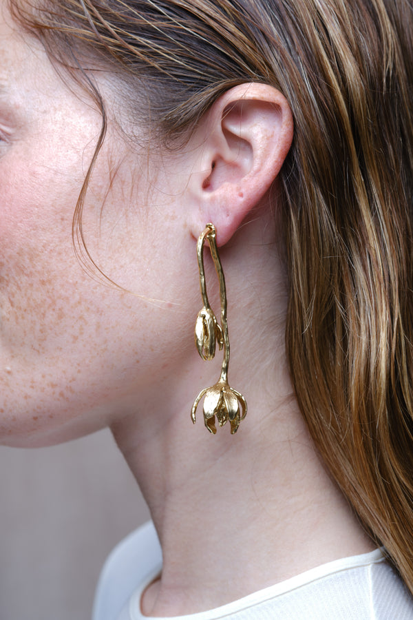 Gold sculptural flower drop earrings worn on model side view