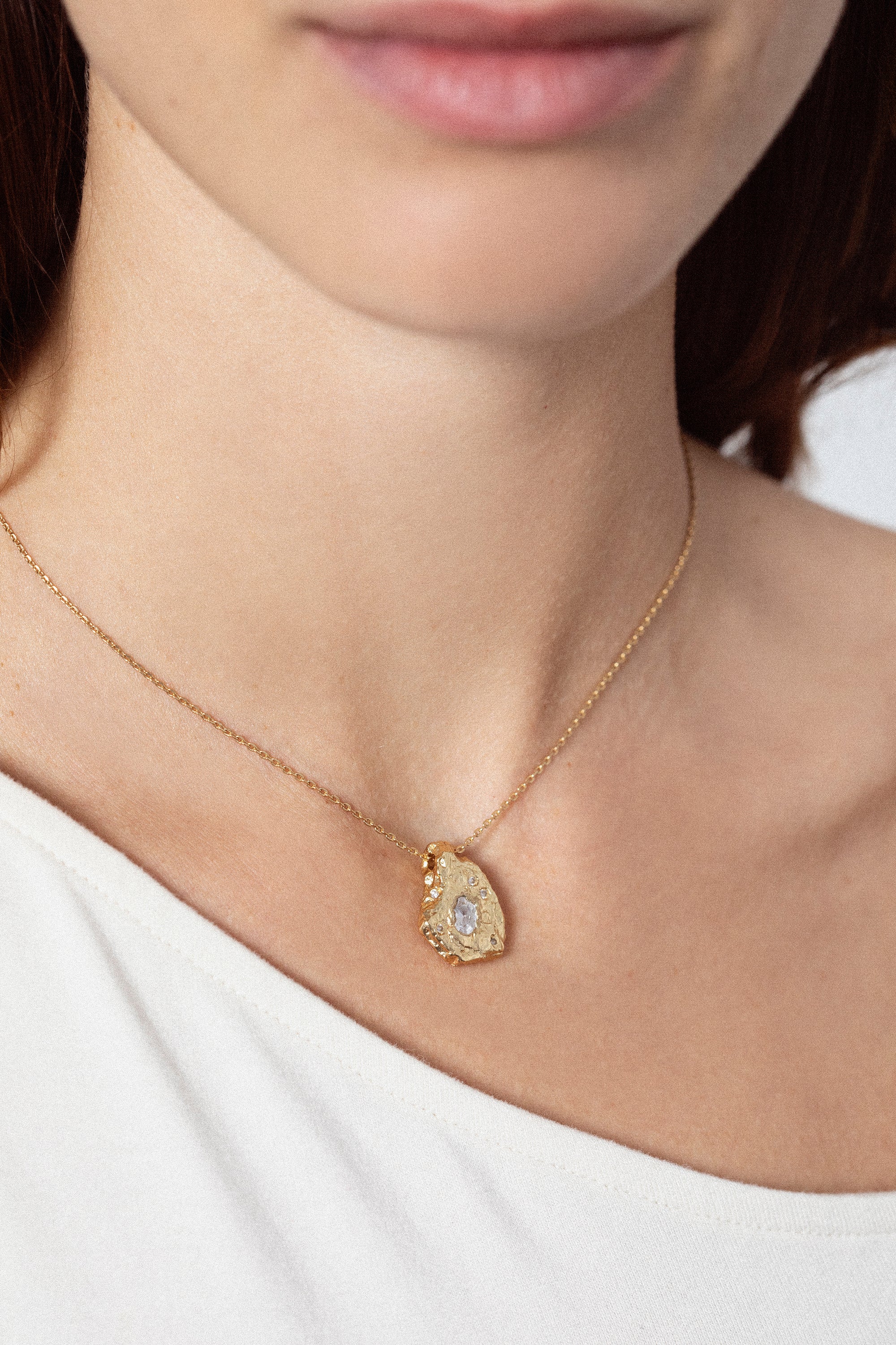 Gold textured organic pendant necklace with clear gemstone worn on model