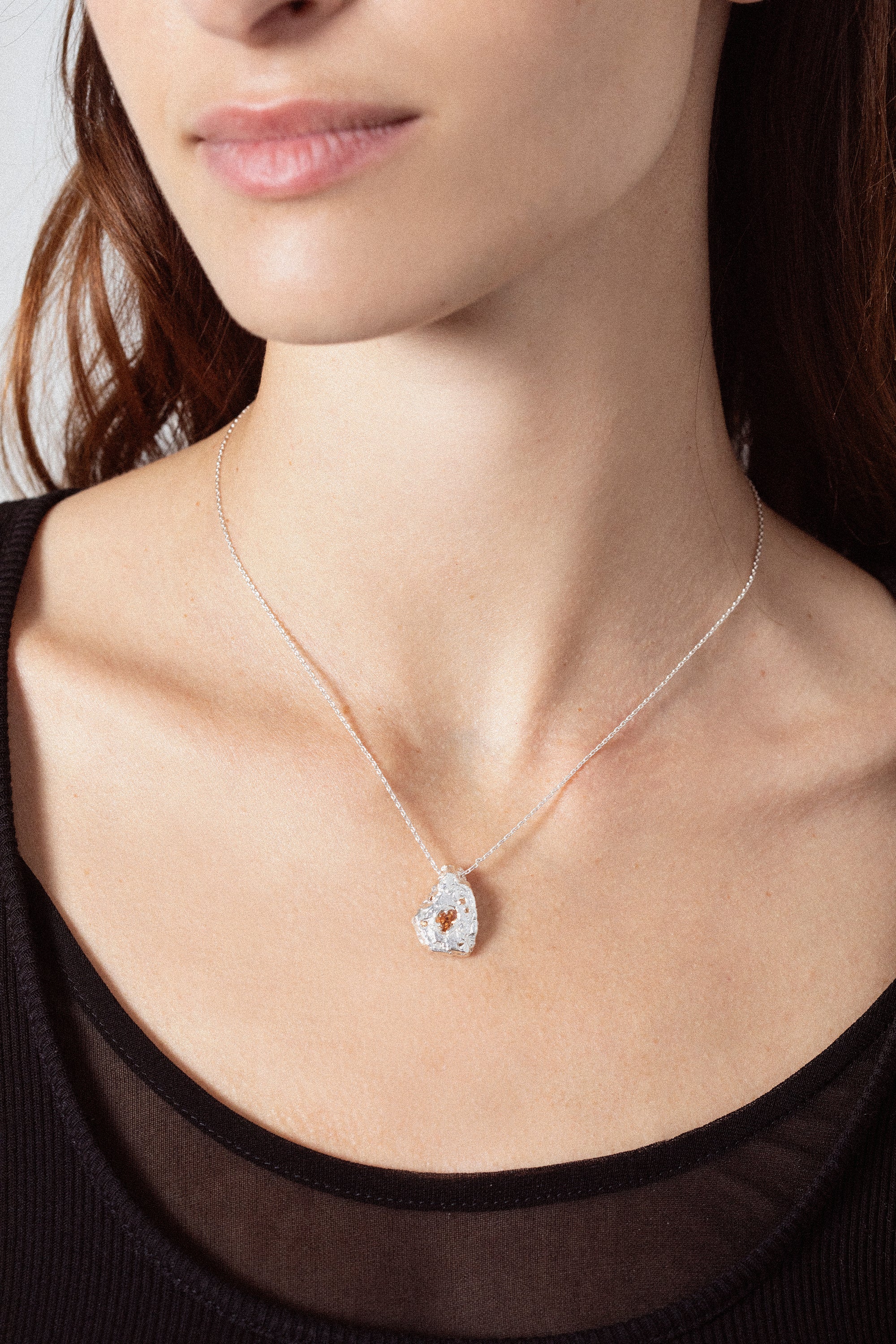 Silver textured organic pendant necklace with clear gemstone worn on model