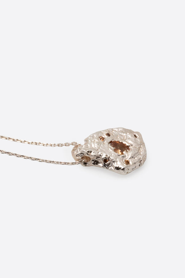 Detail of silver textured organic pendant with clear gemstone