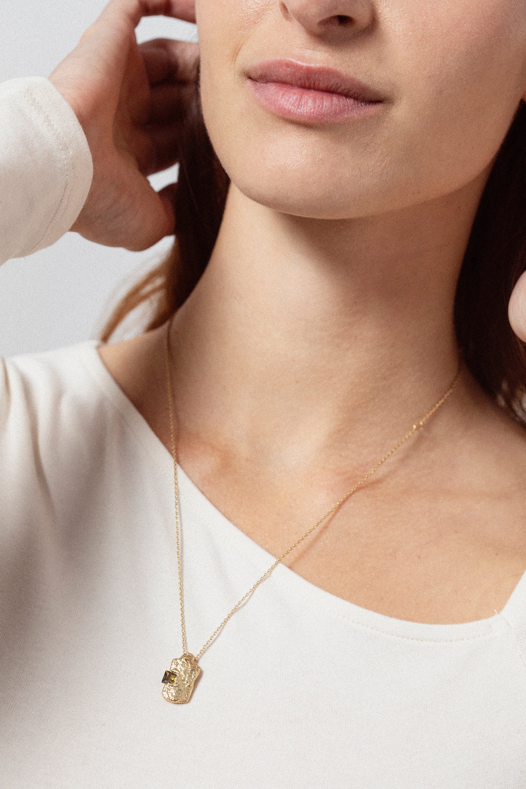 Gold textured rectangular pendant necklace with dark gemstone worn on model