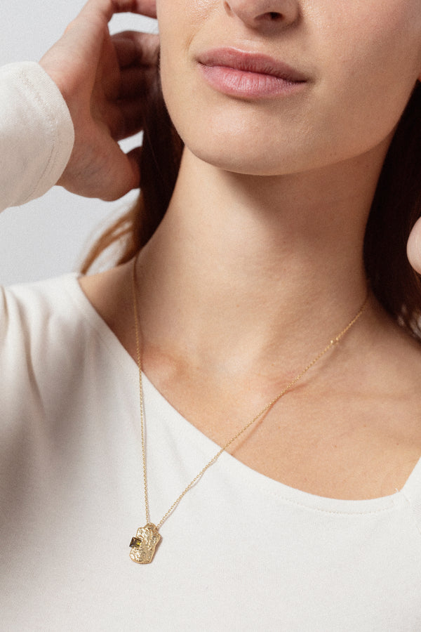Gold textured rectangular pendant necklace with dark gemstone worn on model