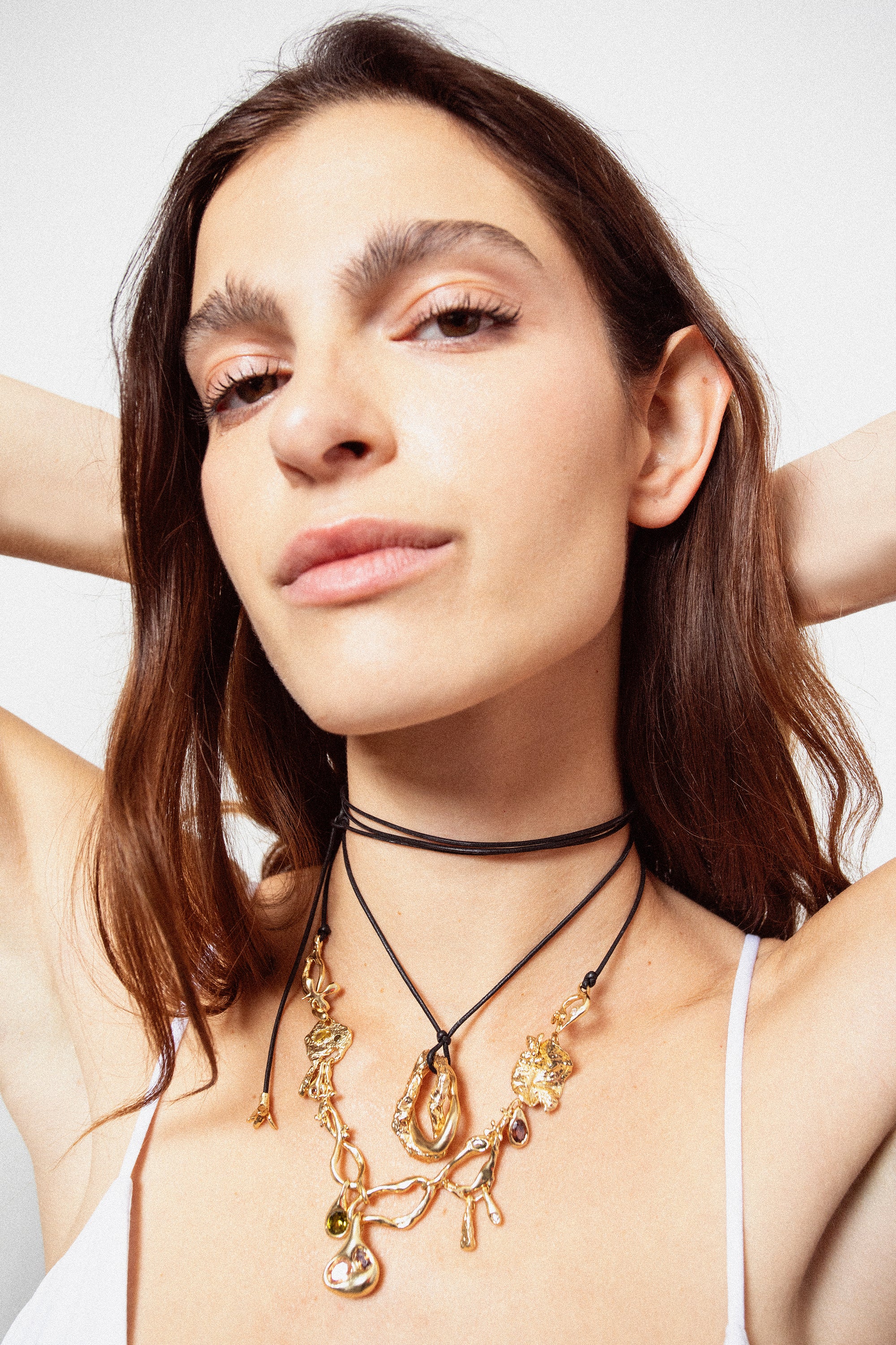 Woman wearing layered gold pendant necklaces on black cords