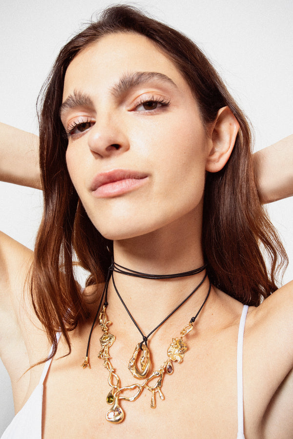 Woman wearing layered gold pendant necklaces on black cords