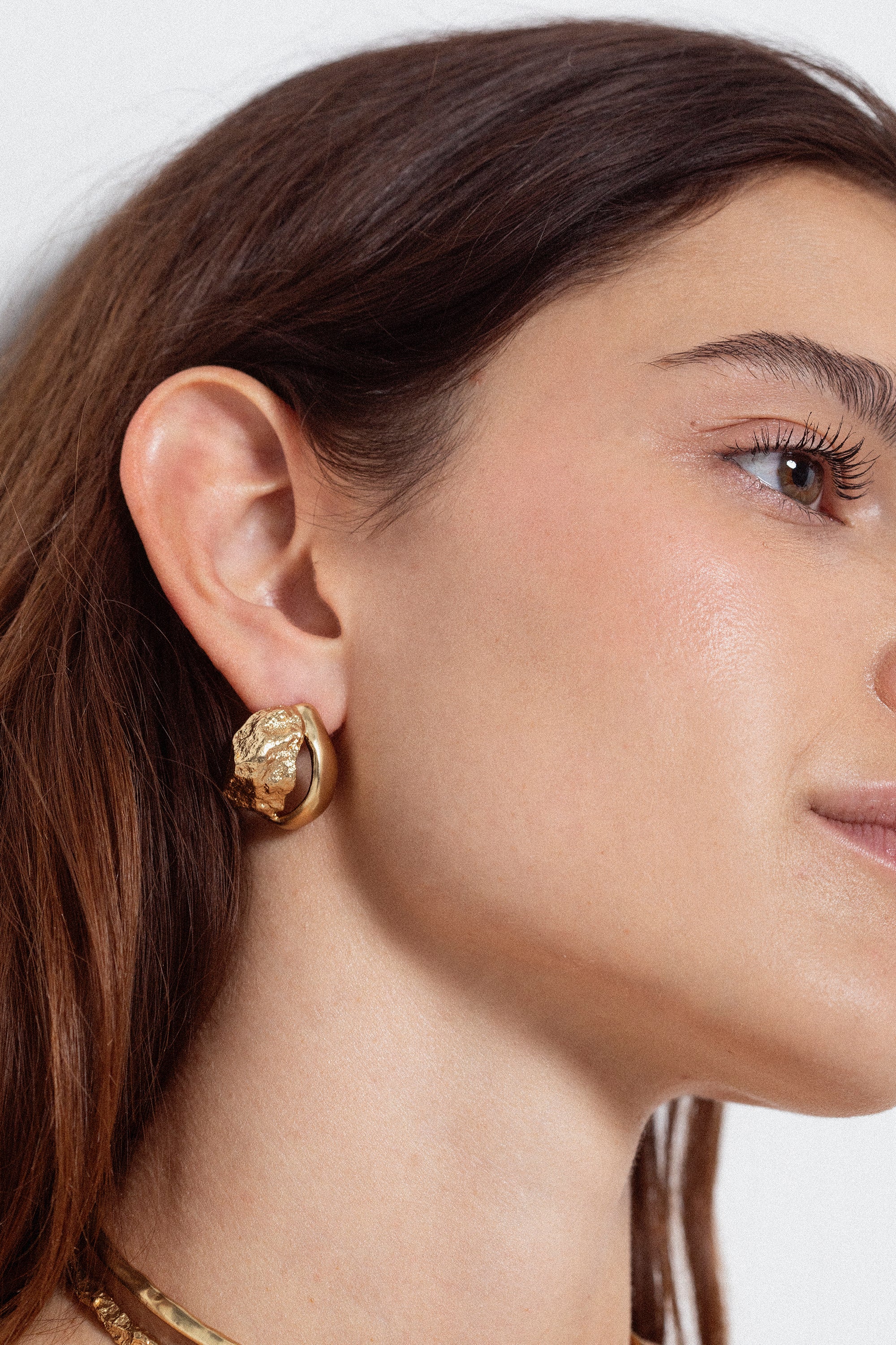 Close-up of woman wearing sculptural gold stud earring with organic textured design