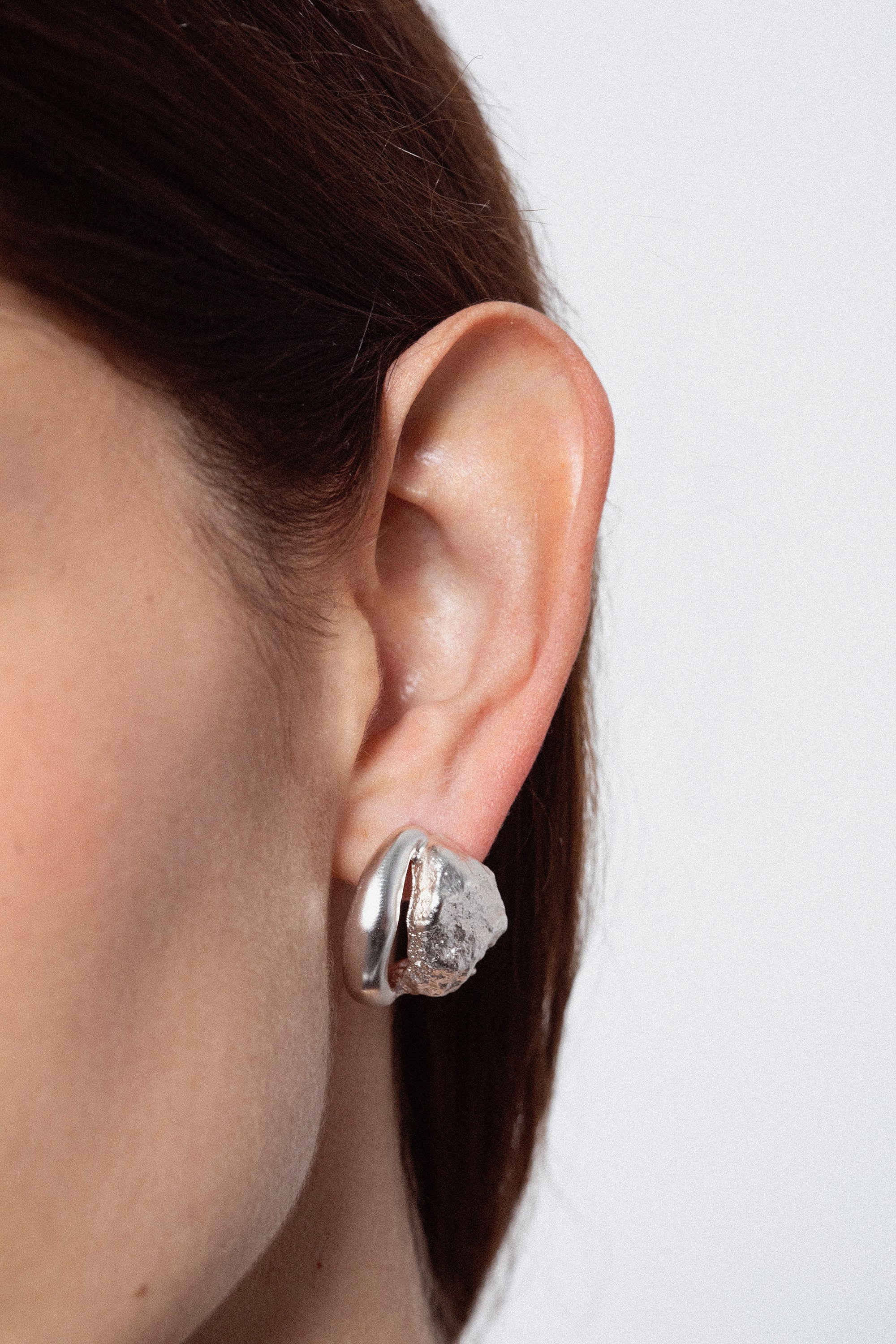 Close-up of woman wearing sculptural silver stud earring with organic textured design