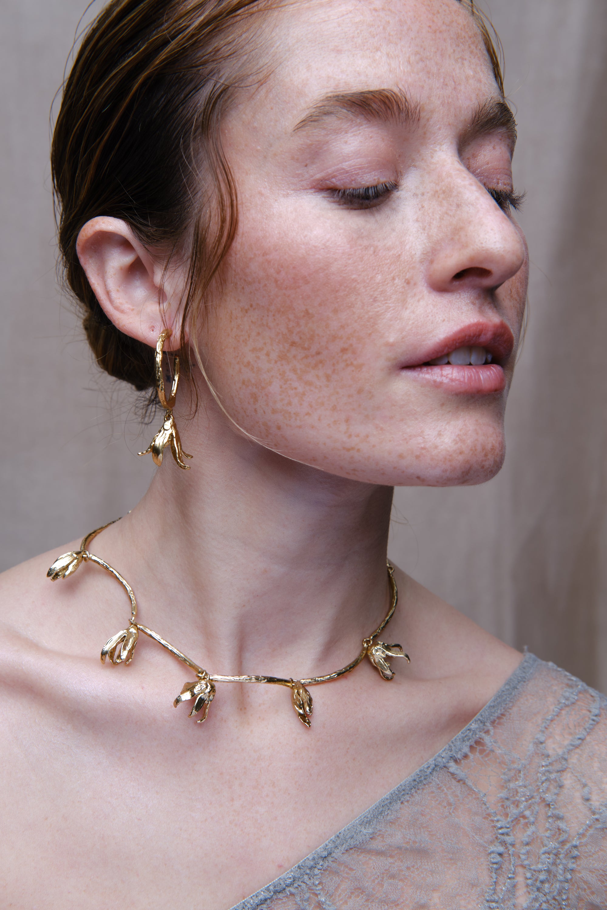 Close-up portrait of woman wearing sculptural gold necklace and matching organic drop earrings
