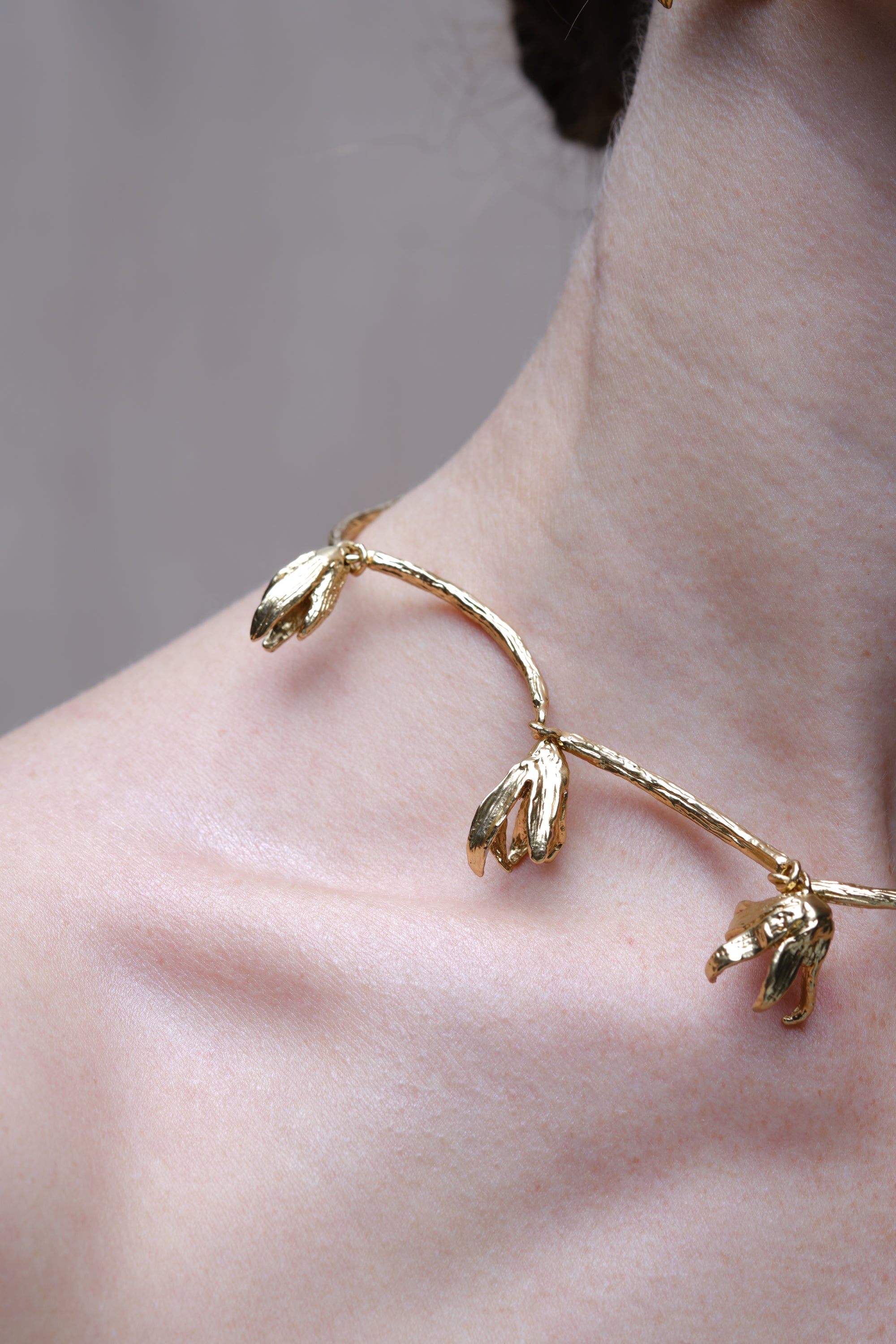 Close-up detail of sculptural gold necklace with organic leaf-shaped elements on skin
