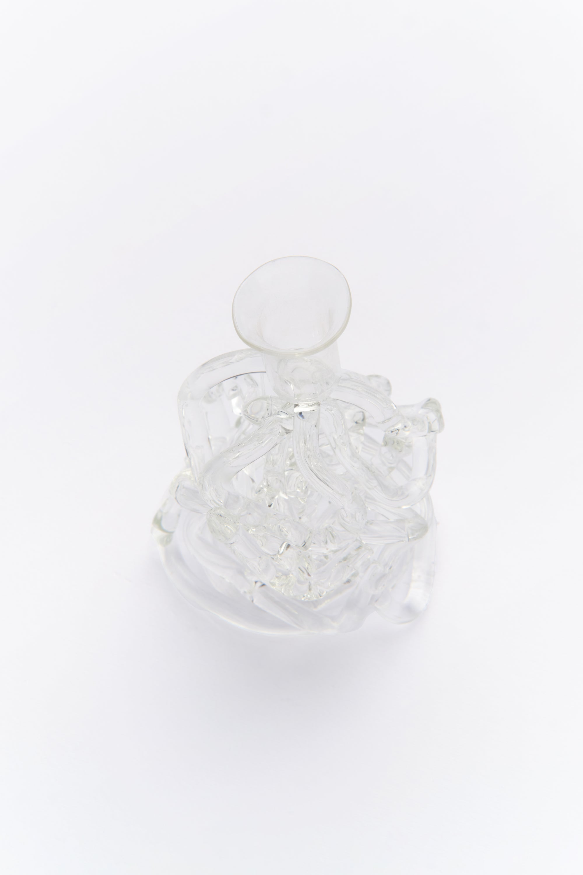 A clear glass candle holder with a sculpted design, resembling the movement of water, displayed with a lit candle on a white surface.