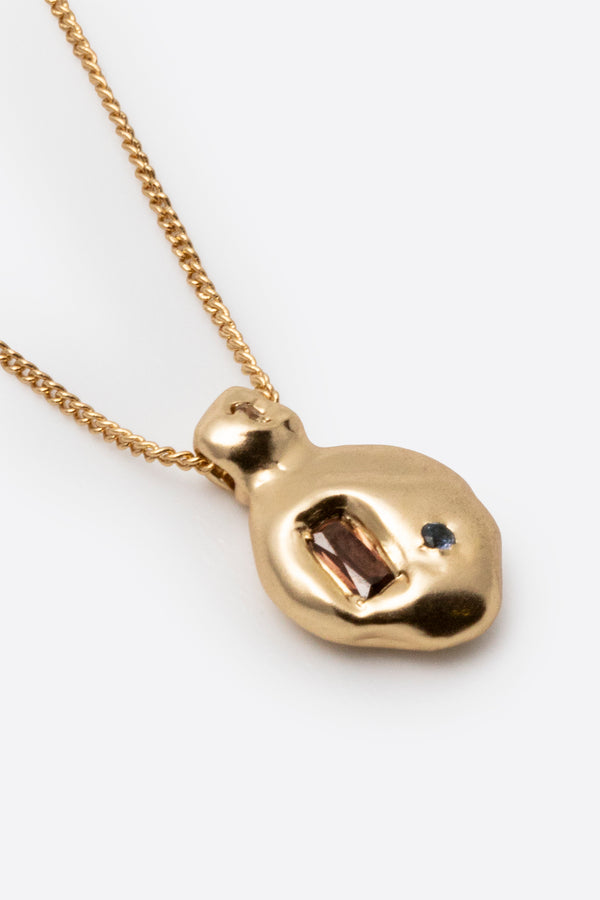 Close-up of gold pendant necklace with dark gemstone and textured setting