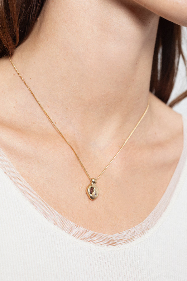 Woman wearing long gold pendant necklace with dark gemstone