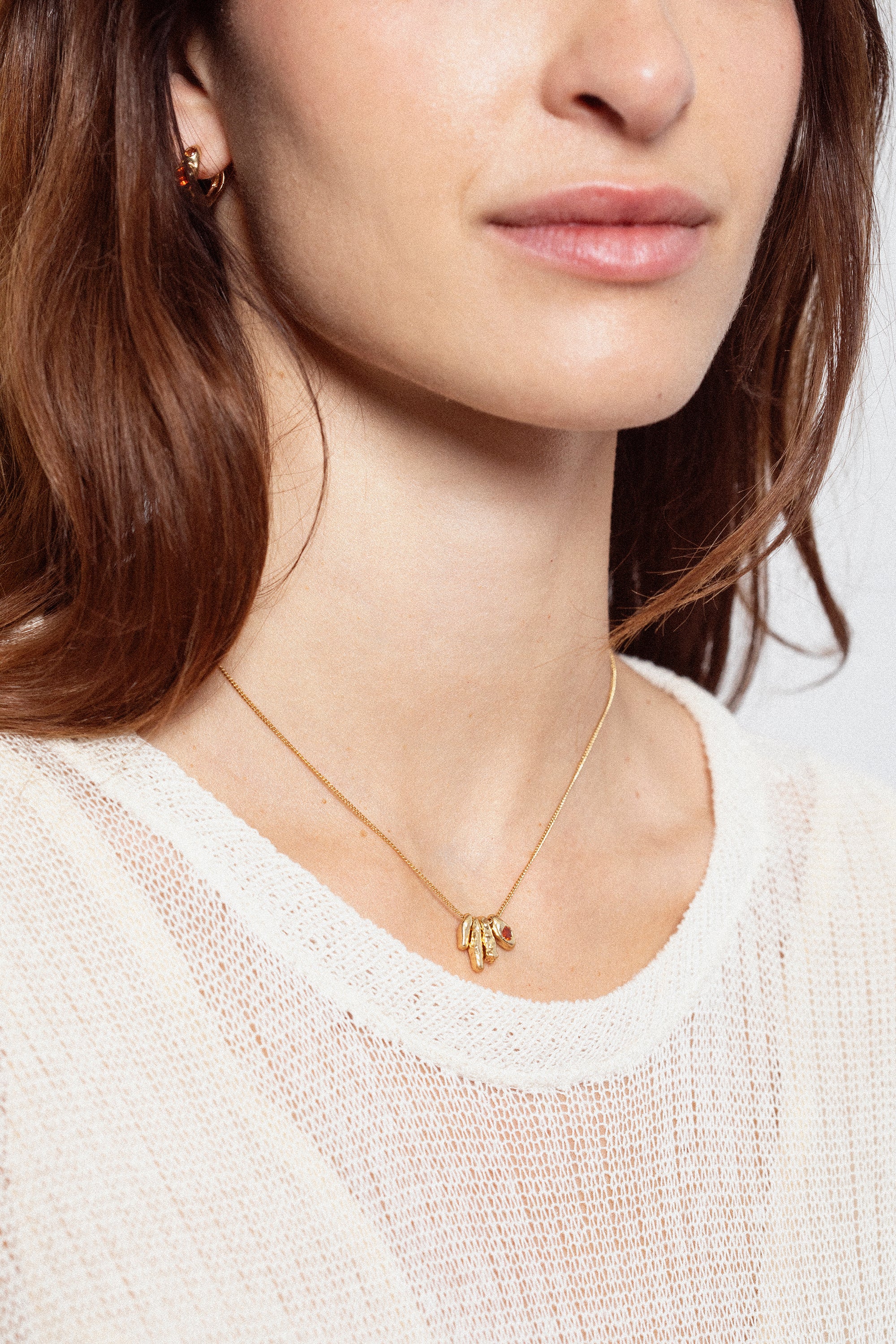 Woman wearing sculptural gold pendant necklace with orange gemstone