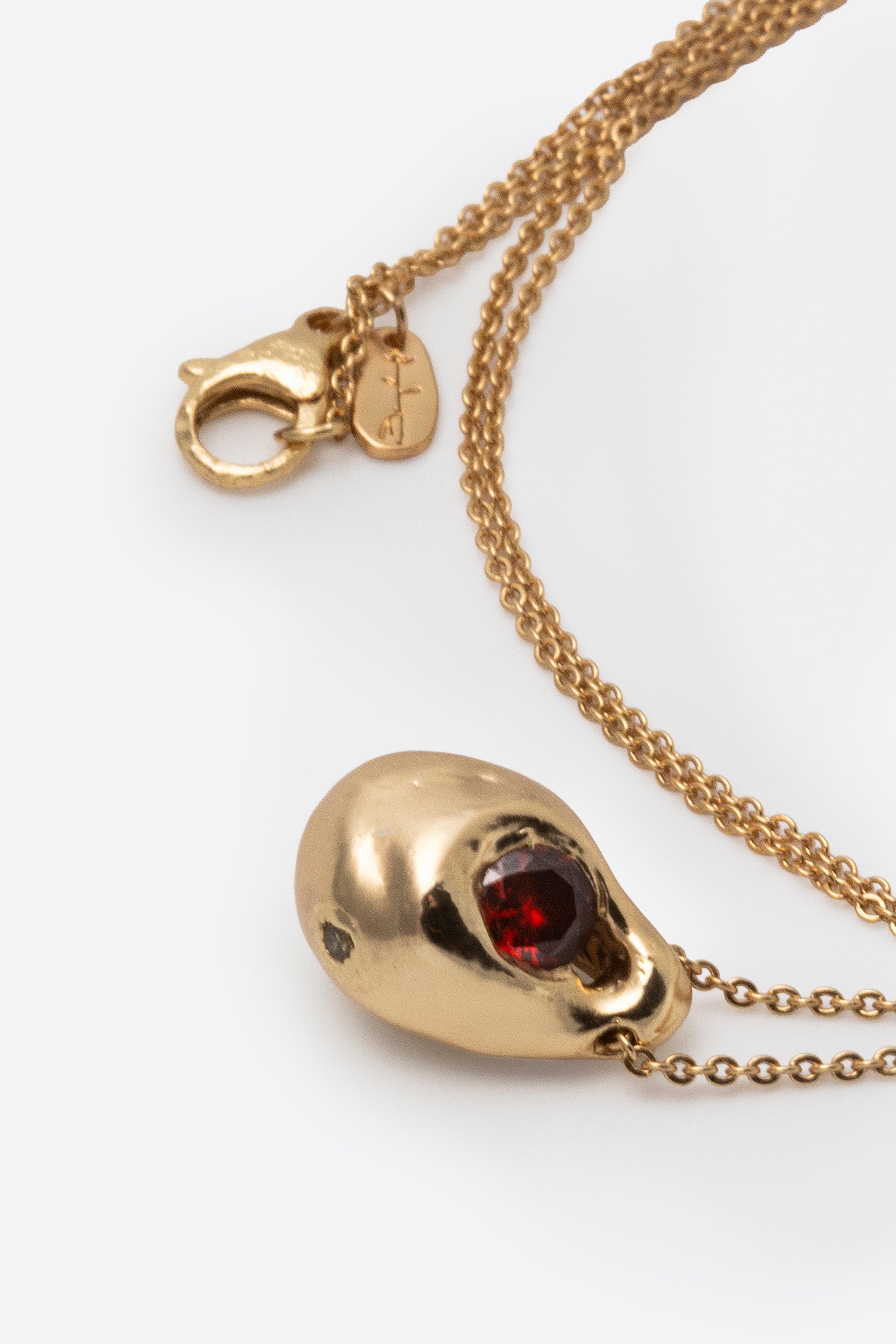 Close-up of gold pendant necklace with dark gemstone and textured setting