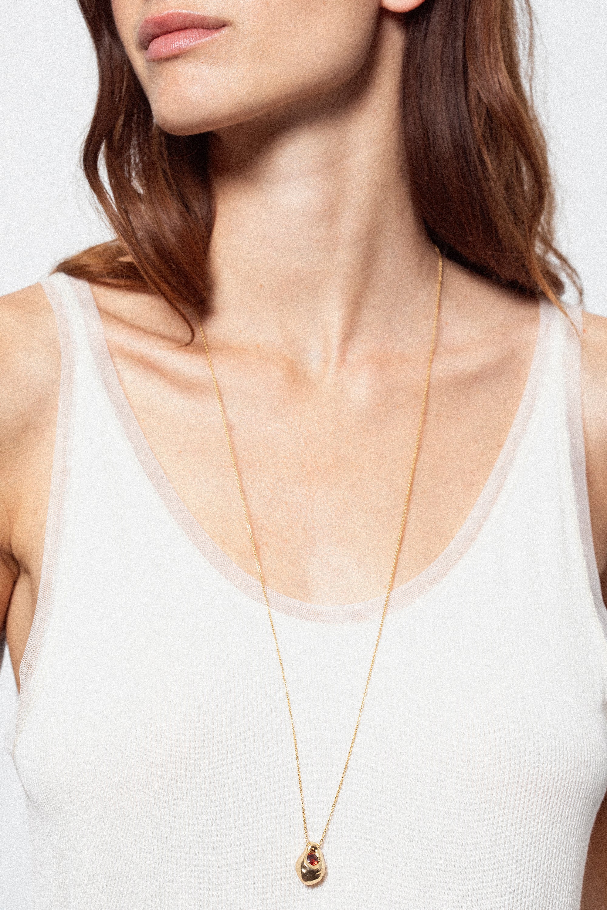 Model wearing long sculptural gold pendant necklace with dark gemstone detail