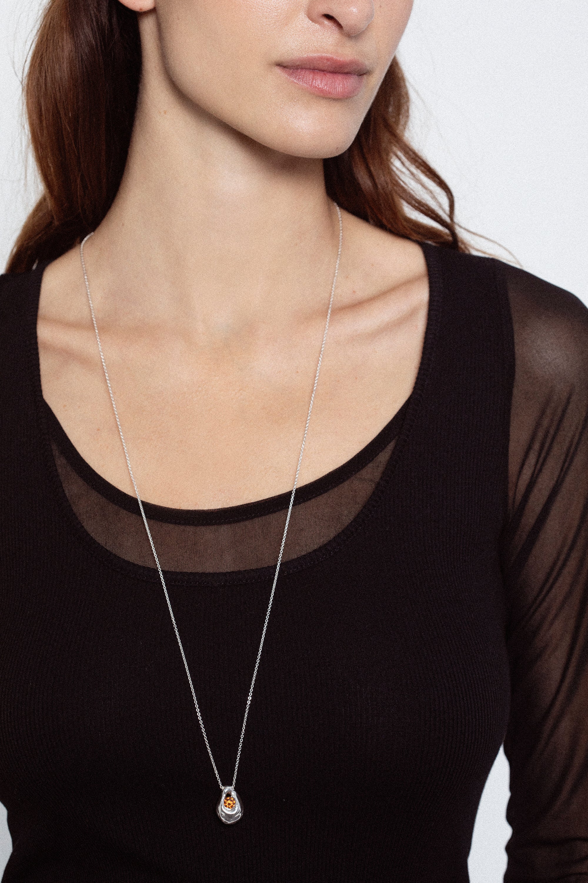 Woman wearing long silver pendant necklace with dark gemstone