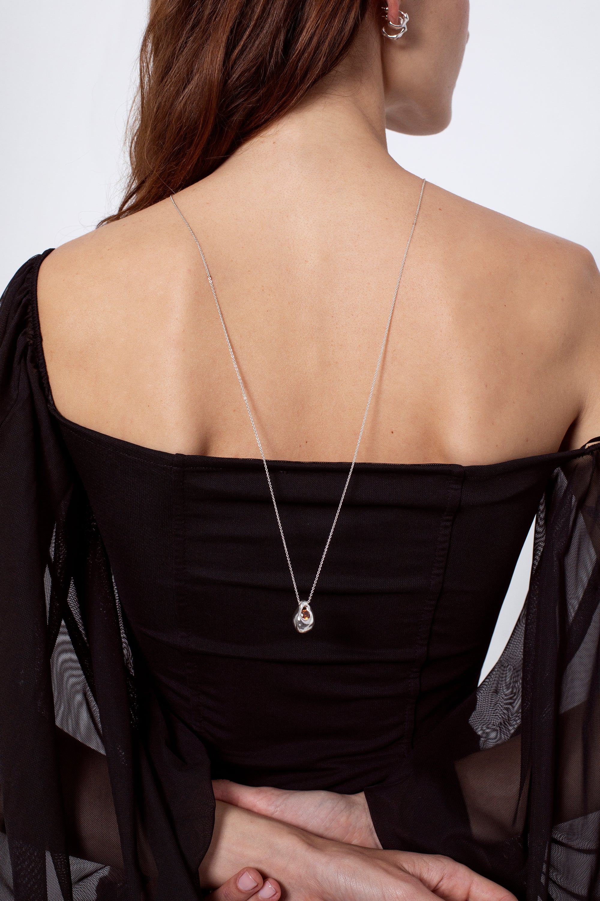 Back view of woman wearing long silver pendant necklace