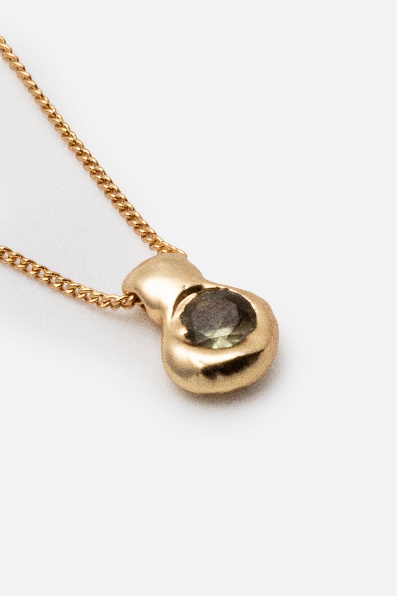 Close-up of gold pendant necklace with dark gemstone and textured setting