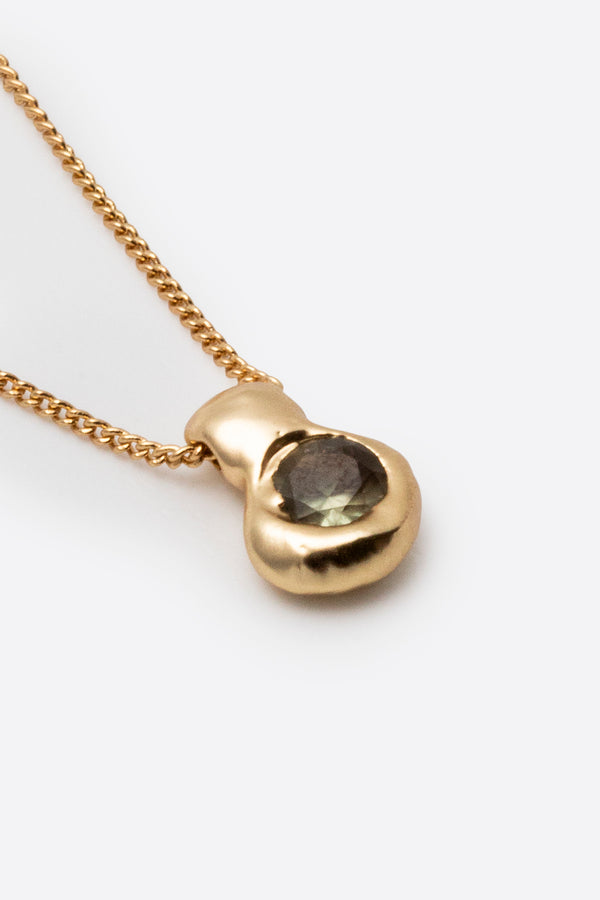 Close-up of gold pendant necklace with dark gemstone and textured setting