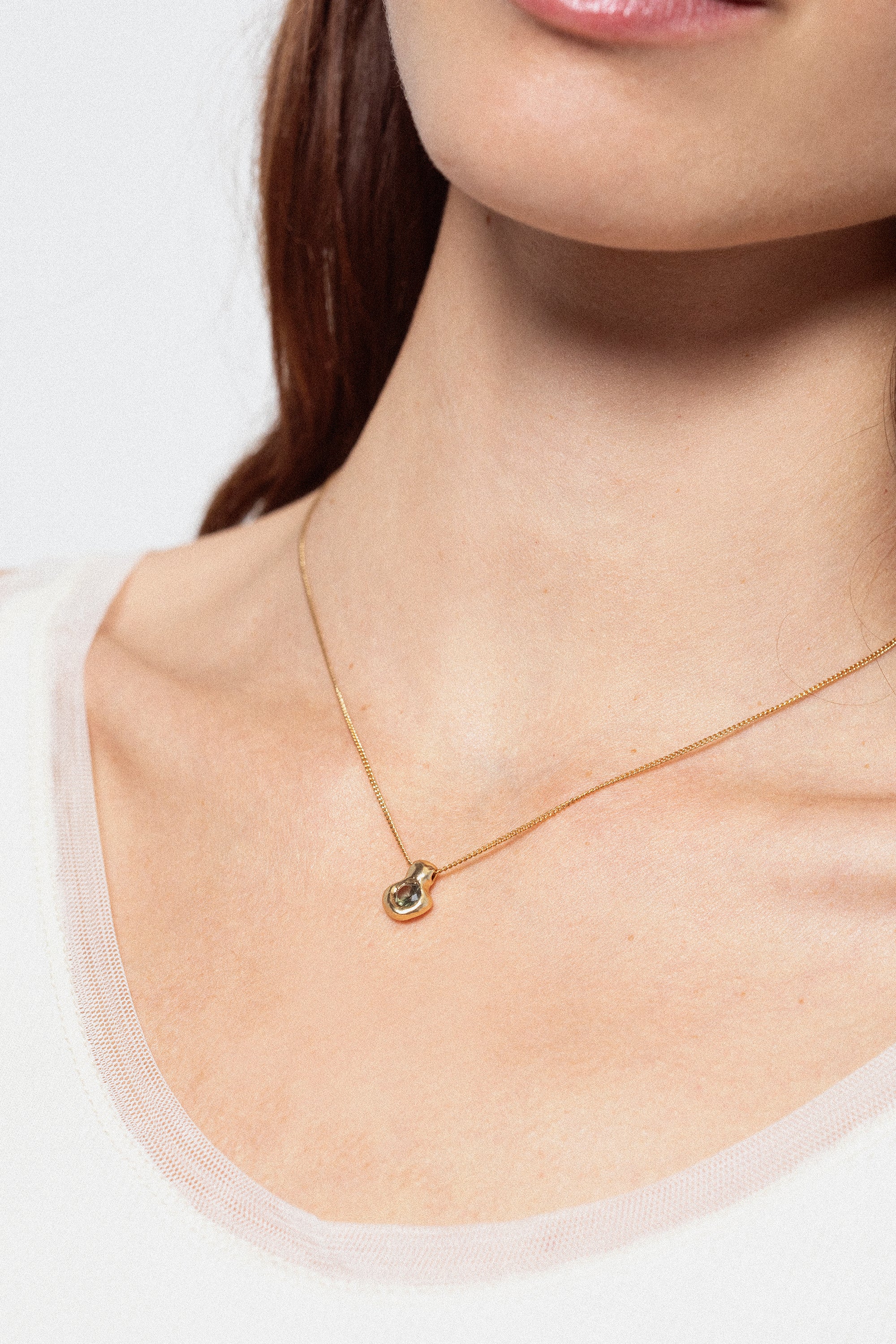 Woman wearing gold pendant necklace with dark gemstone detail