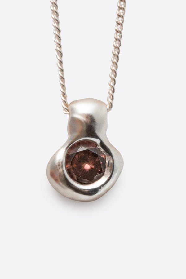 Close-up of silver pendant necklace with dark gemstone and textured setting