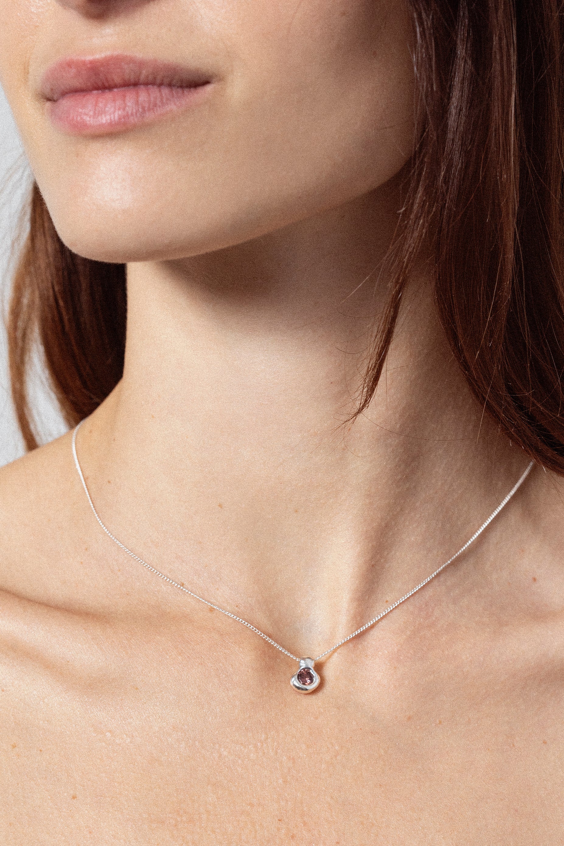 Woman wearing sculptural silver pendant necklace with dark gemstone
