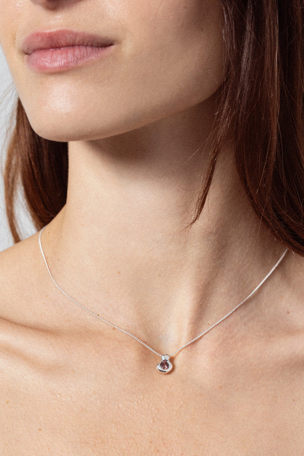 Woman wearing sculptural silver pendant necklace with dark gemstone