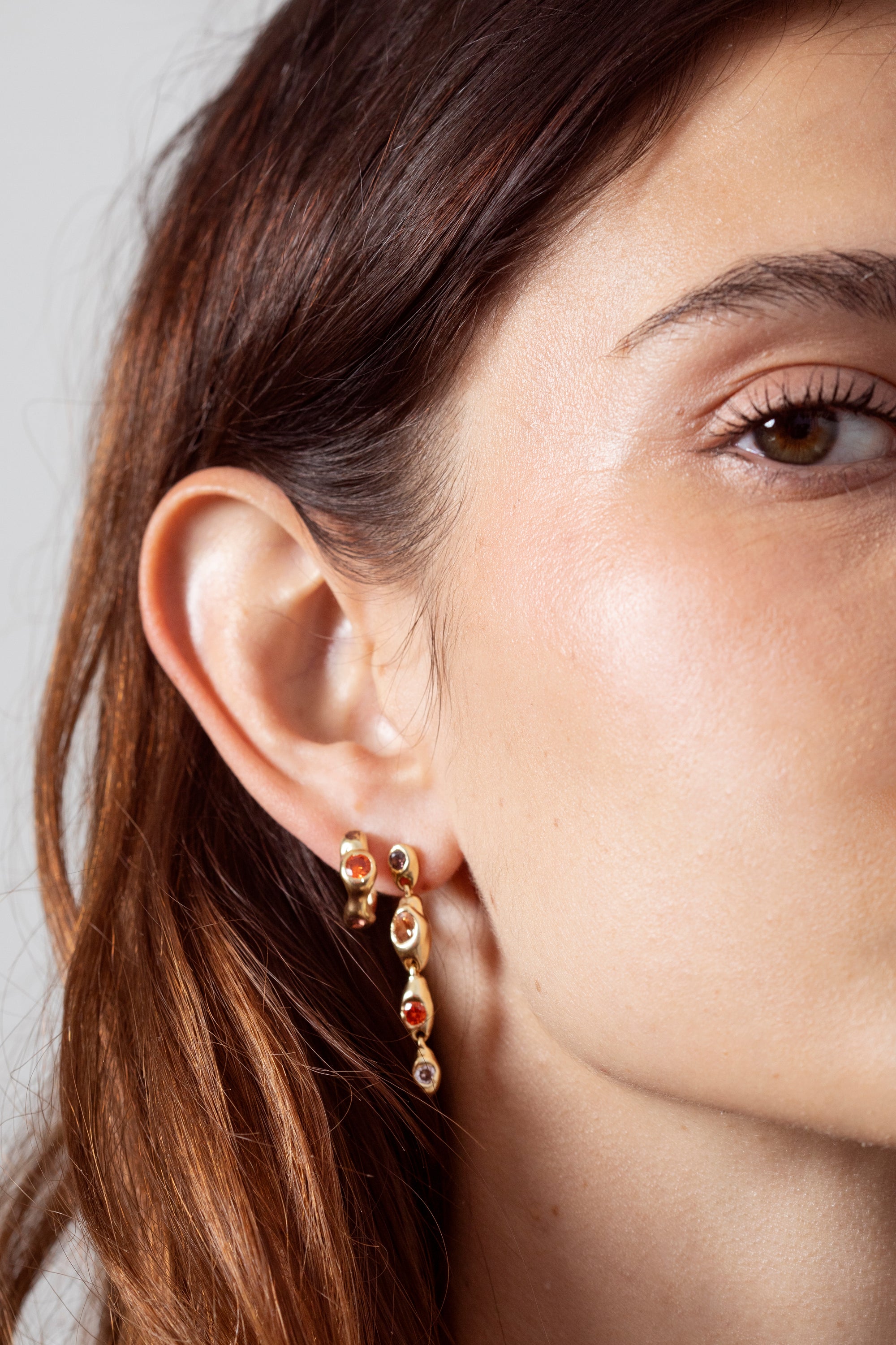 Woman wearing sculptural gold gemstone huggie earrings