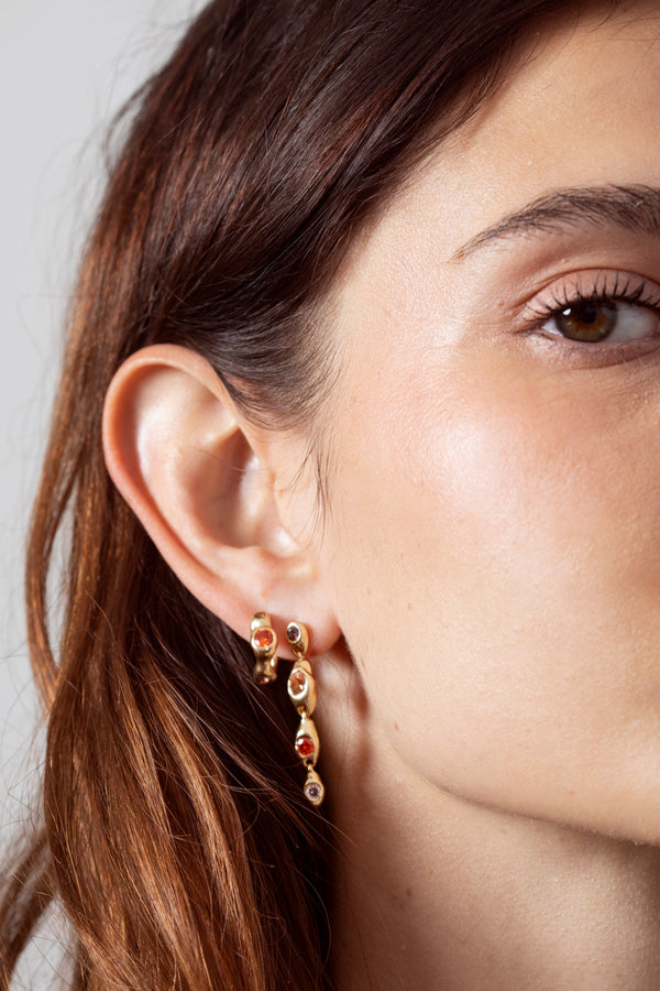 Woman wearing sculptural gold gemstone huggie earrings