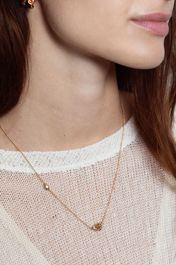 Woman wearing sculptural gold gemstone pendant necklace on fine chain