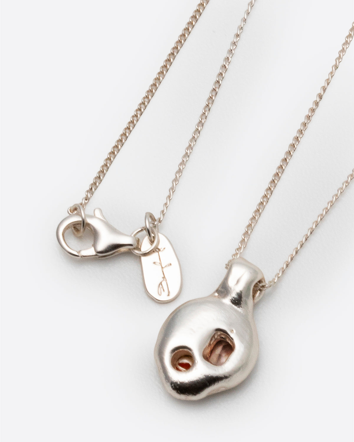 Ambar Necklace in silver: rounded pendant with two inset stones beside the clasp and brand tag.
