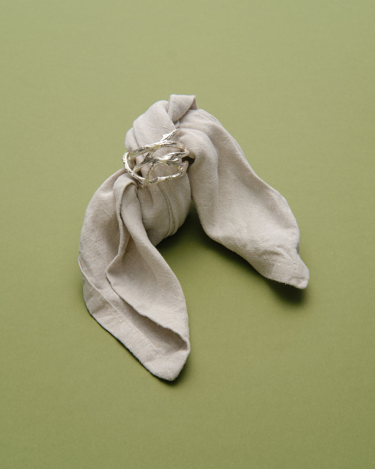 Autumn Cutlery Napkin Ring in silver: napkin ring holding a pale fabric napkin on a green background.