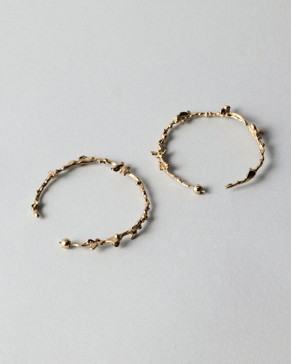 Butterflies Dance Hoops in gold: pair of large irregular textured hoop earrings on a pale background.