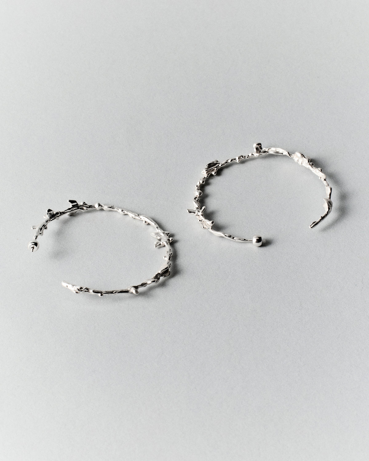 Butterflies Dance Hoops in silver: pair of large irregular textured hoop earrings on a pale background.