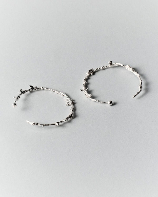 Butterflies Dance Hoops in silver: pair of large irregular textured hoop earrings on a pale background.