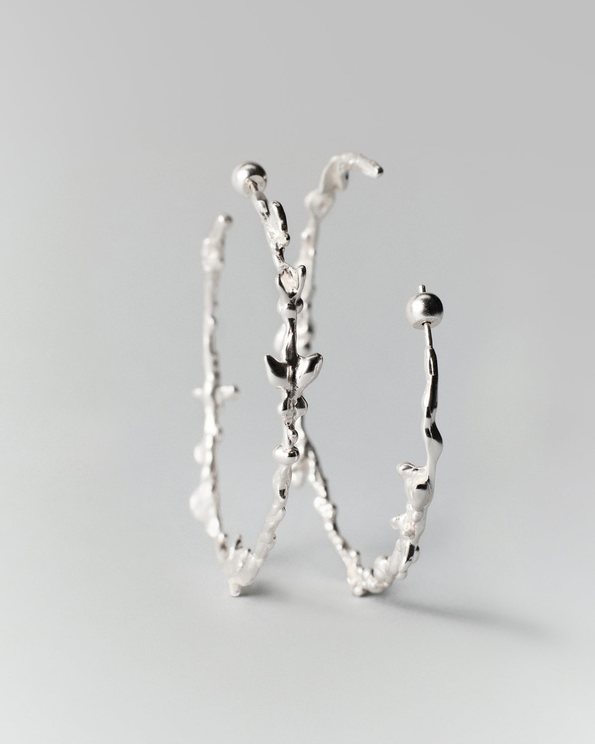 Butterflies Dance Hoops in silver: hoop earrings standing upright to show their irregular profiles.