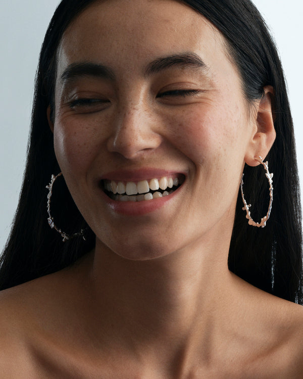 Butterflies Dance Hoops in silver: smiling model wearing large irregular hoop earrings.