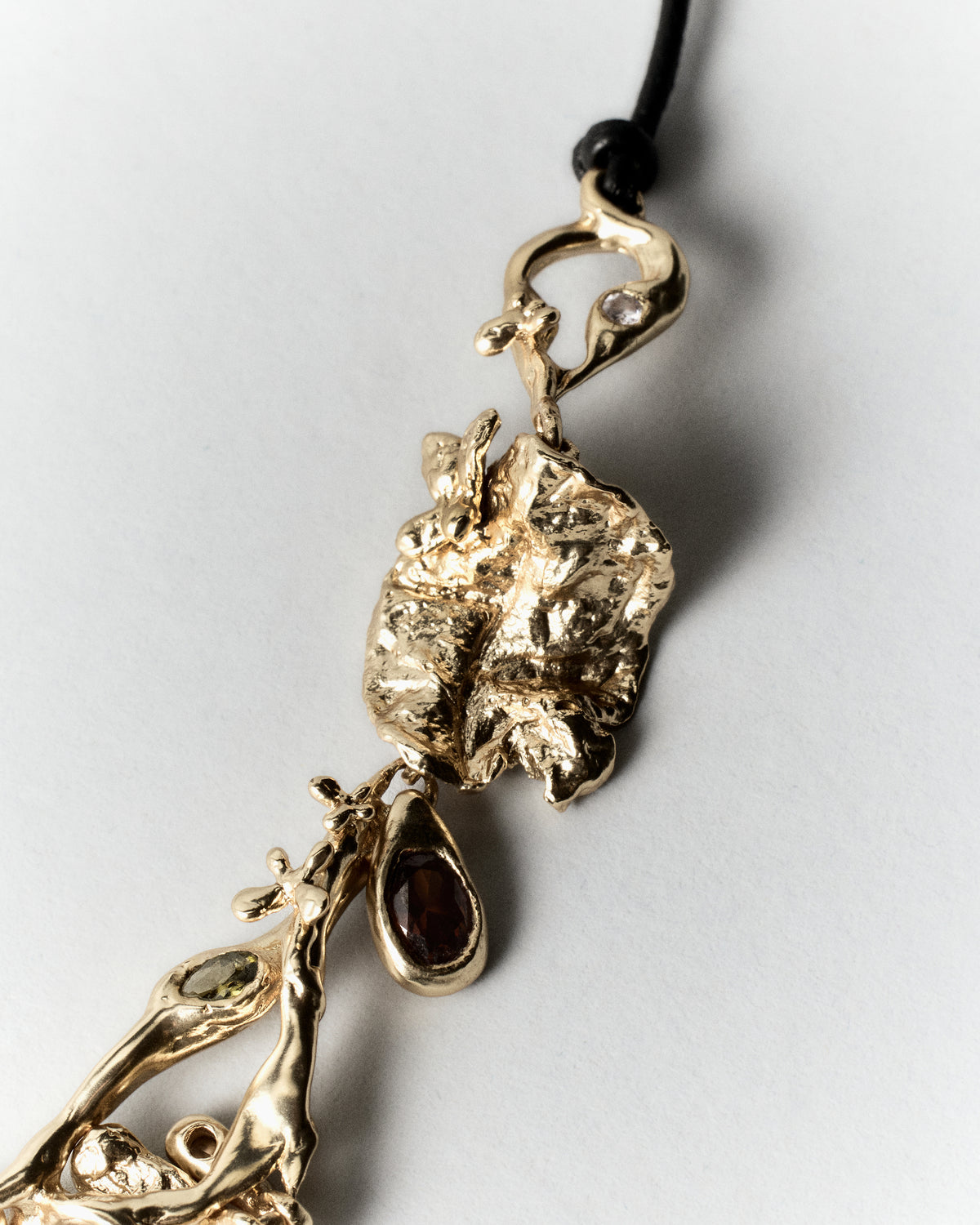 Cocoon Necklace in gold: detail of the necklace's textured charm and black cord.