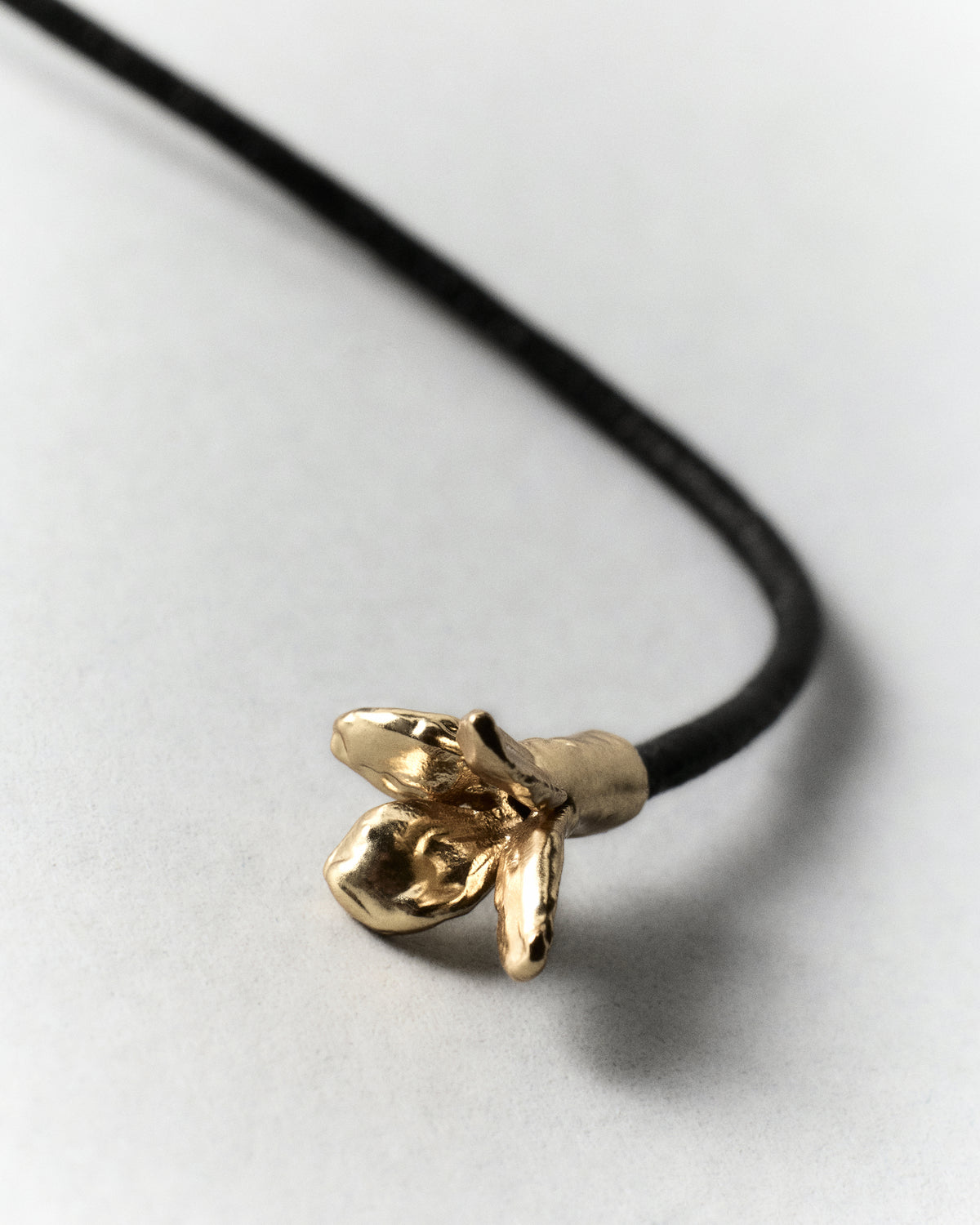 Cocoon Necklace in gold: close-up of the decorative metal end on the black cord.