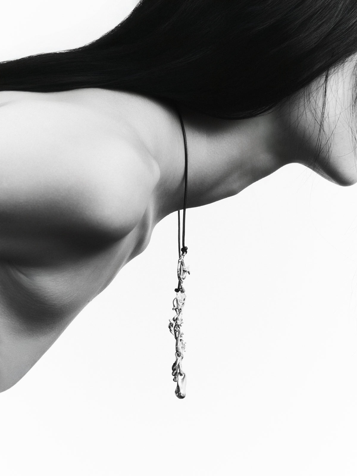 Cocoon Necklace in gold: black-and-white close-up of dangling sculptural jewelry beside a model's neck.
