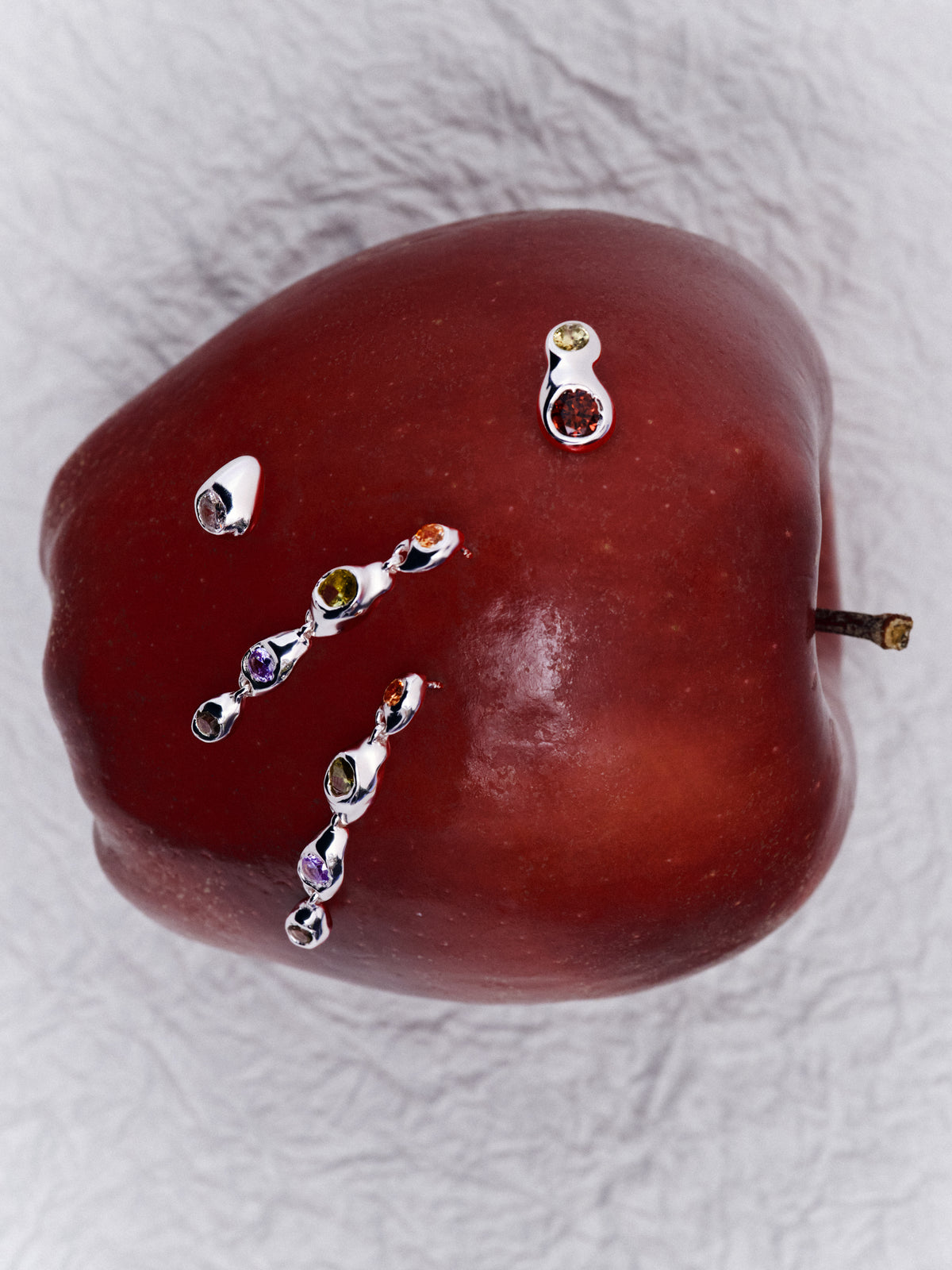 Double Pepita Studs Earrings in silver: stud earrings and other small jewelry arranged on a red apple.