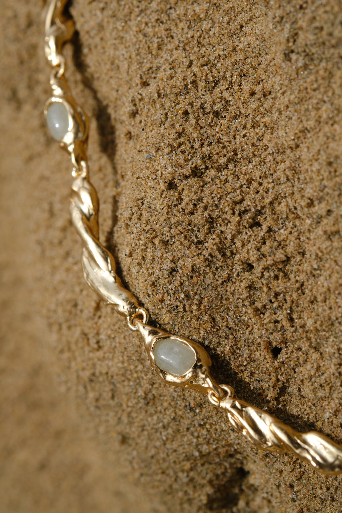 Dunestone Necklace in gold: necklace with pale stones arranged on rough brown fabric.