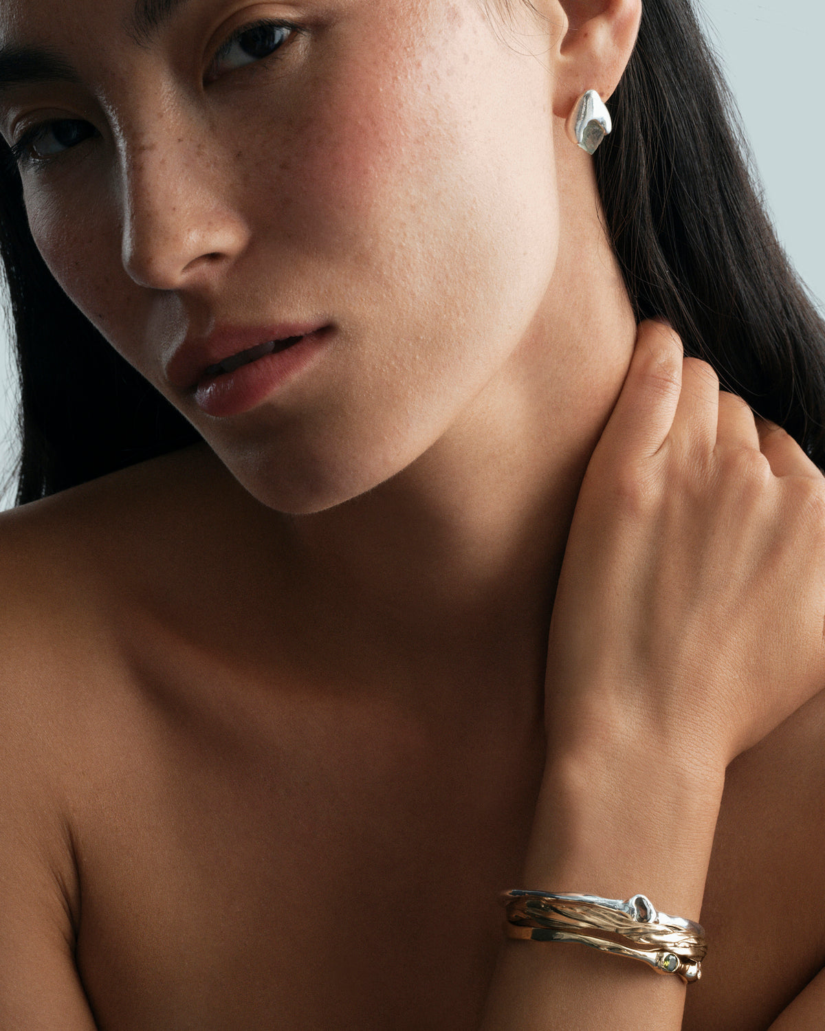 Flourita Earrings in silver: portrait of a model wearing a rough-stone stud and layered cuff bracelets.