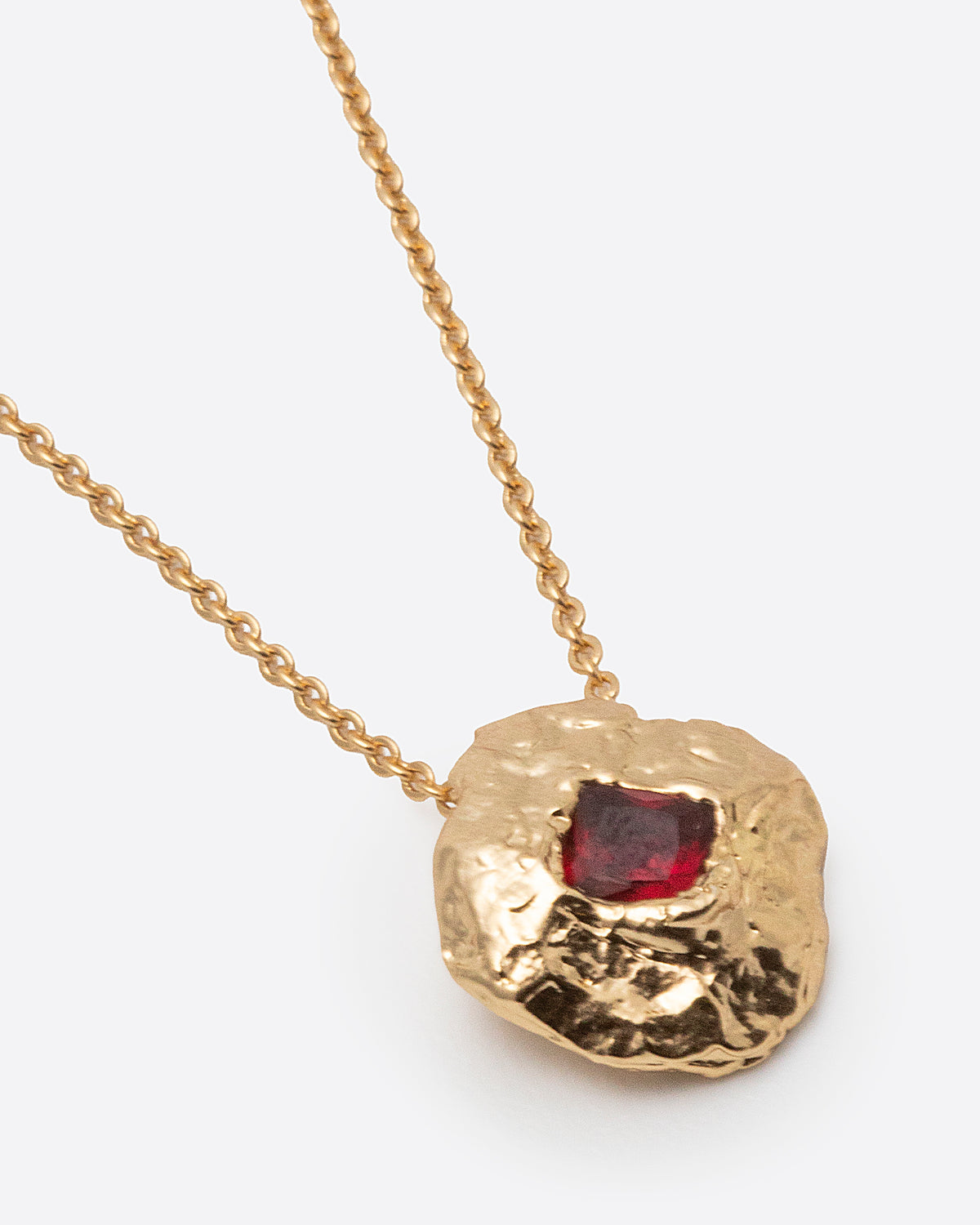 Helios Necklace in gold: close-up of the irregular round pendant with a red rectangular stone.