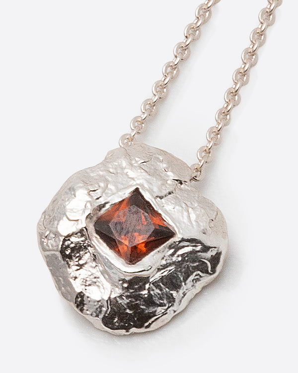 Helios Necklace in silver: close-up of the irregular round pendant with a reddish rectangular stone.