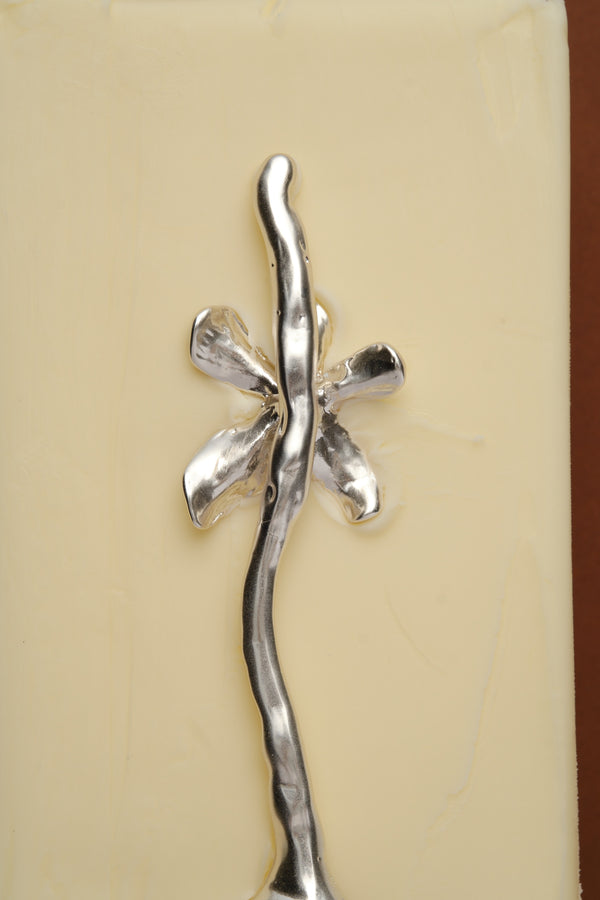 Close-up detail of sculptural silver spoon with organic floral handle on butter surface