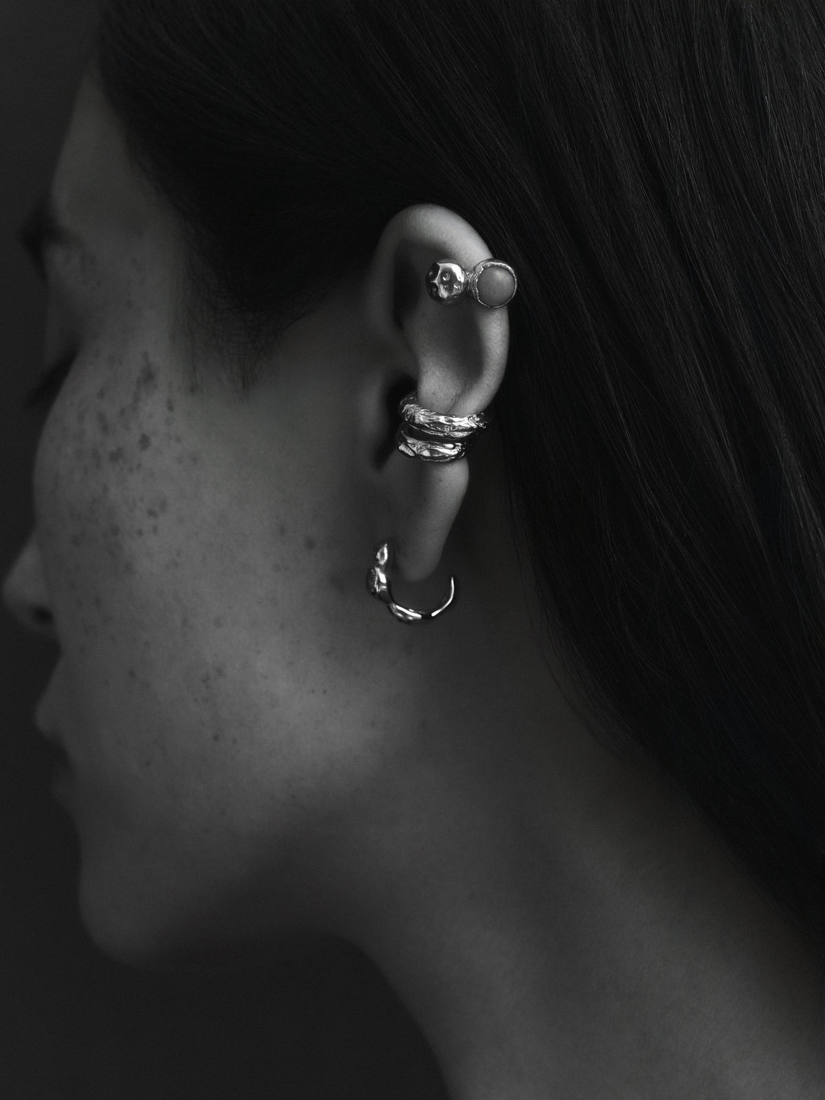 Layered Earth Earcuff in gold: black-and-white close-up of an ear styled with an ear cuff and several earrings.